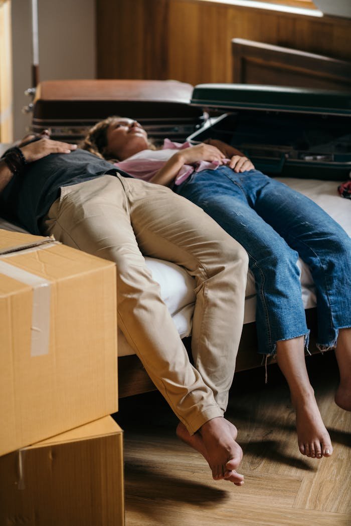 A couple relaxes on a bed surrounded by moving boxes, signifying a new beginning in their home.
